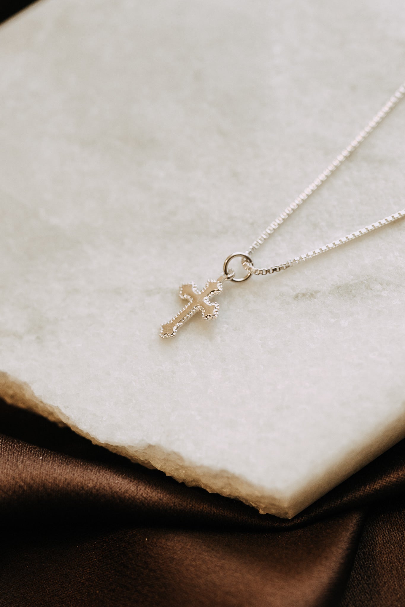 Vintage-inspired silver cross pendant necklace photographed on neutral background