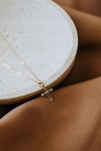 Dainty gold filled cross pendant necklace on cable chain displayed on neutral stone tray