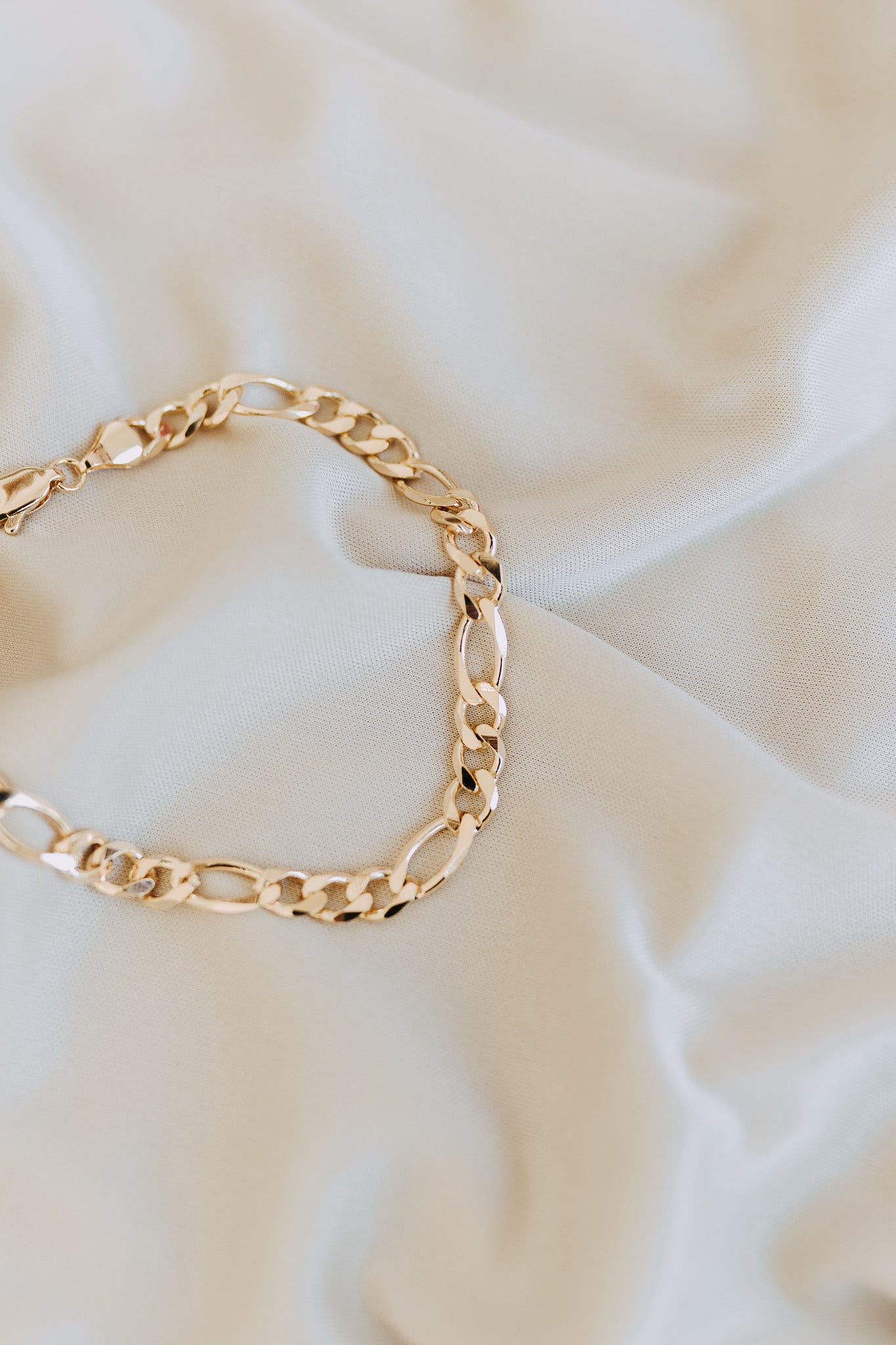 Detailed close-up of polished men’s Figaro chain bracelet on cream fabric background