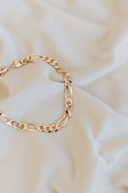 Detailed close-up of polished men’s Figaro chain bracelet on cream fabric background