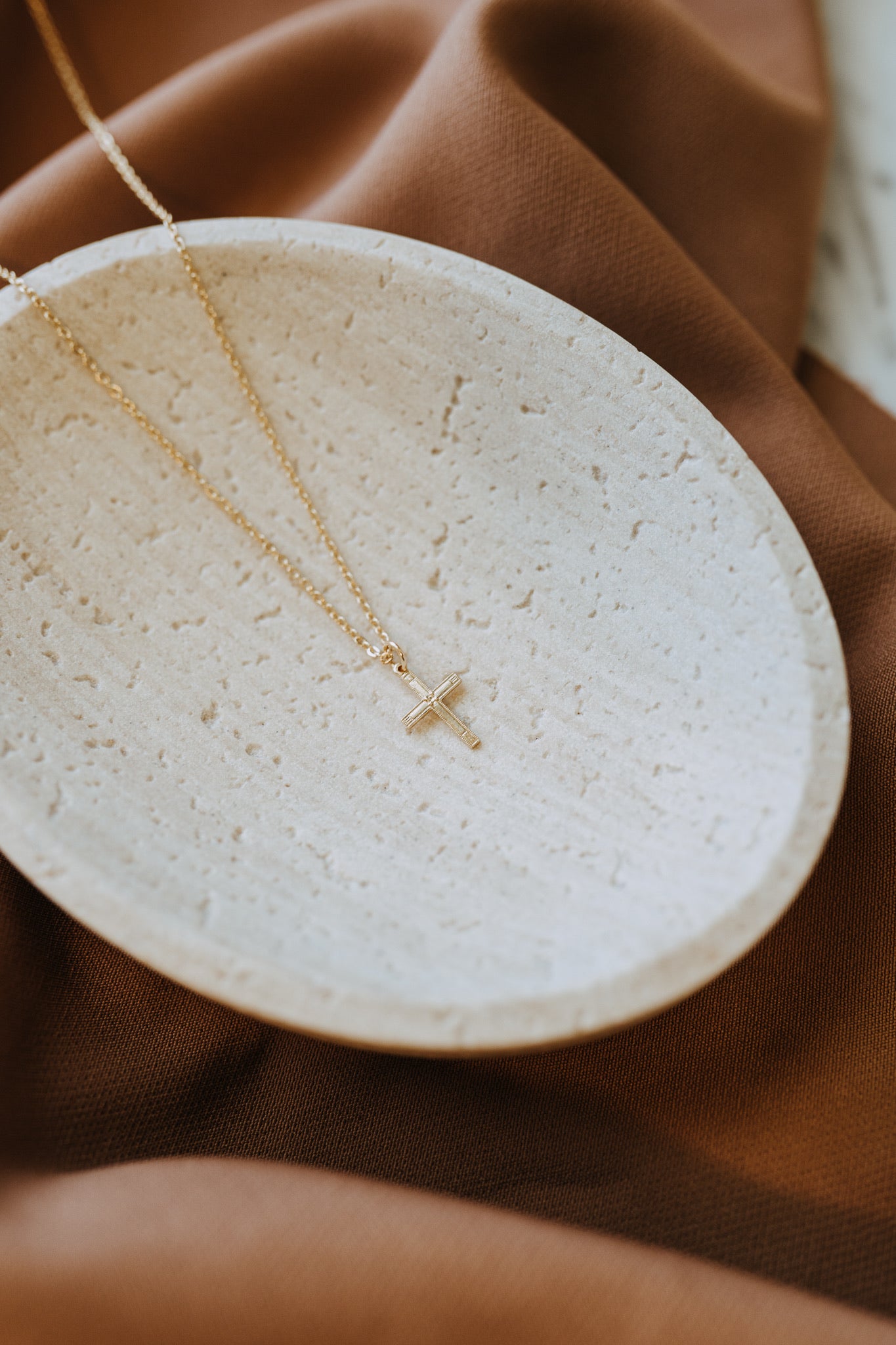 Gold cross pendant necklace photographed on cream stone tray