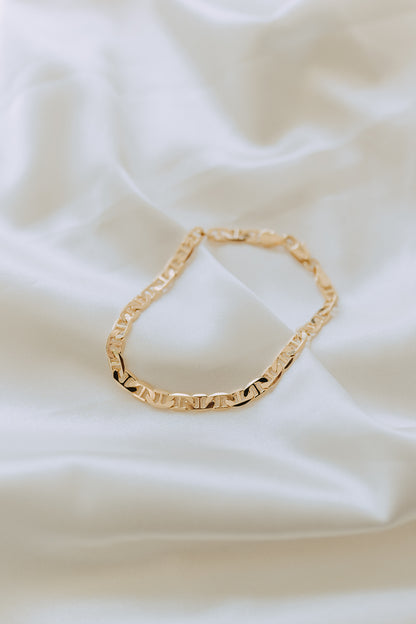 Flat lay of men’s Roma chain bracelet in polished gold on soft white fabric background