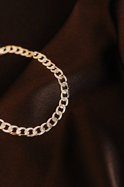 Detailed close-up of men’s curb chain bracelet on dark satin fabric background