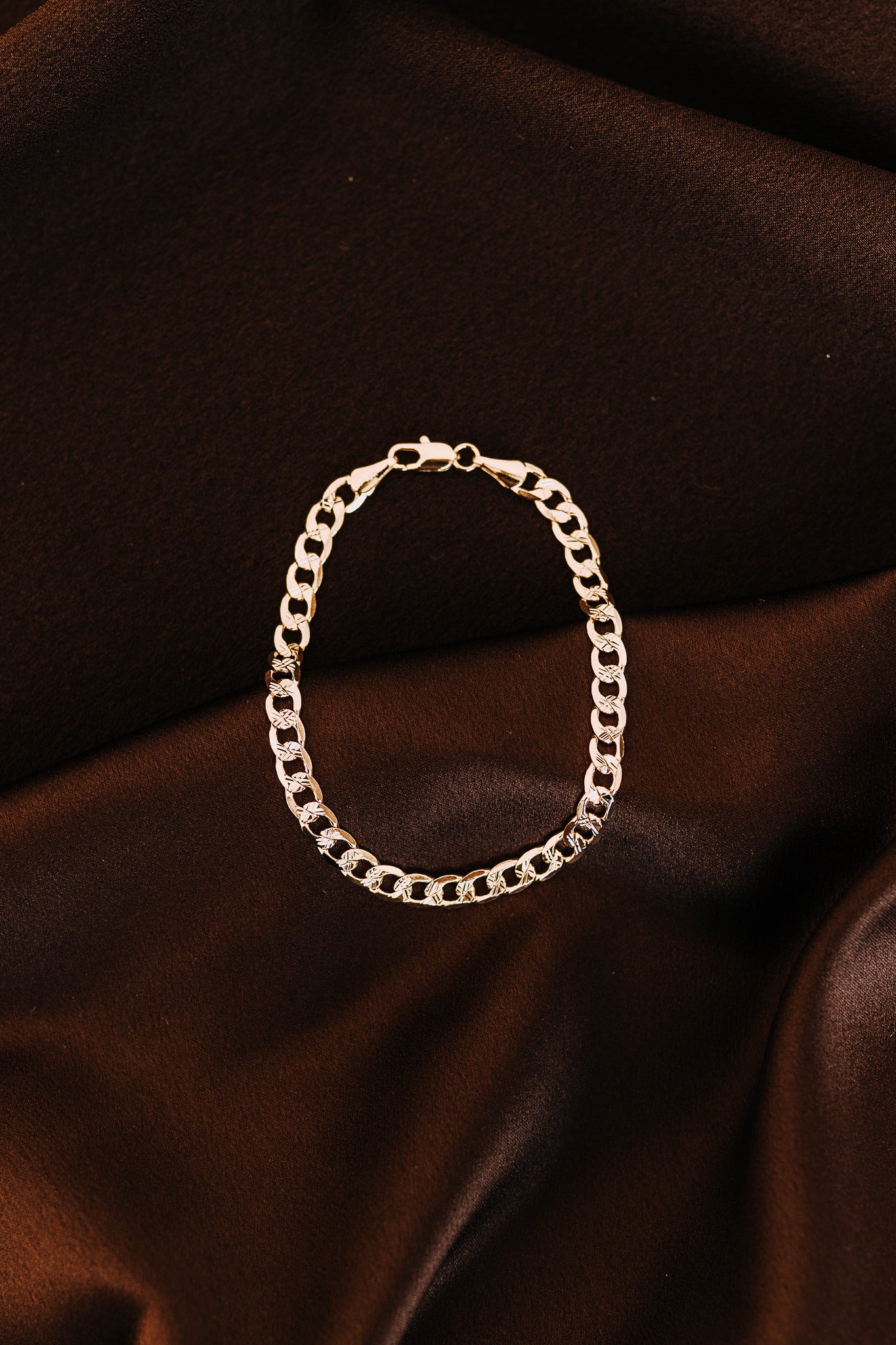Detailed close-up of men’s curb chain bracelet on dark satin fabric background