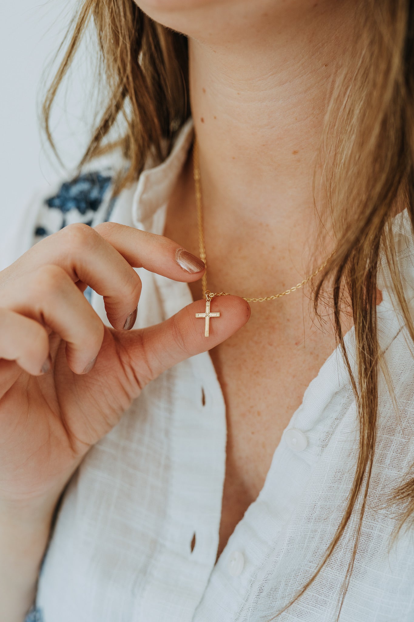 Woman wearing minimalist gold cross on a cable chain necklace 