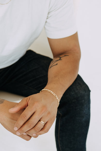 Detailed close-up of polished men’s Figaro chain bracelet on cream fabric background