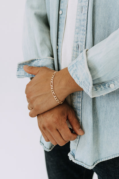 Men’s 6mm Figaro chain bracelet in polished gold worn with casual denim and white tee