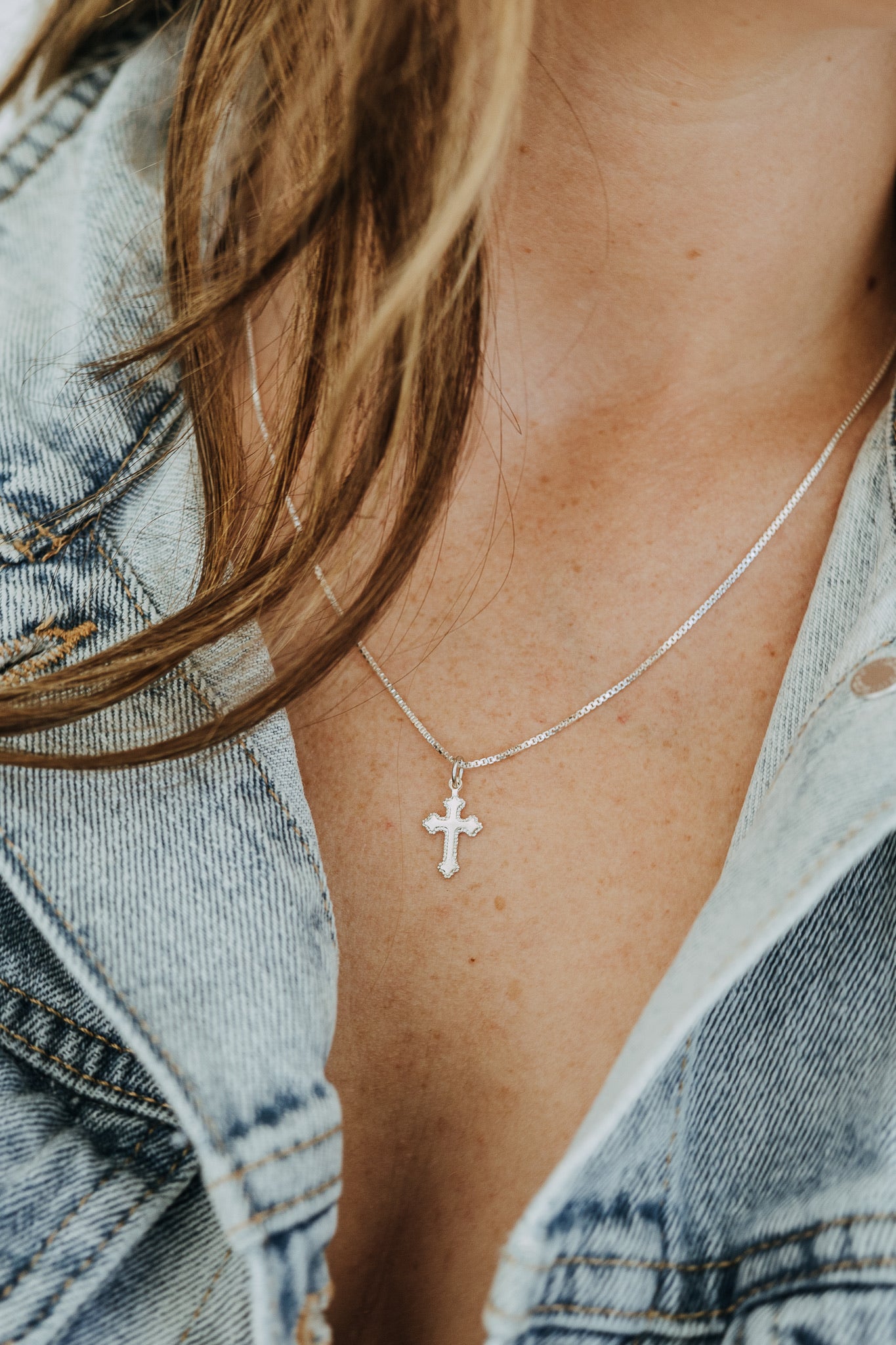 Woman wearing sterling silver cross pendant necklace with denim jacket