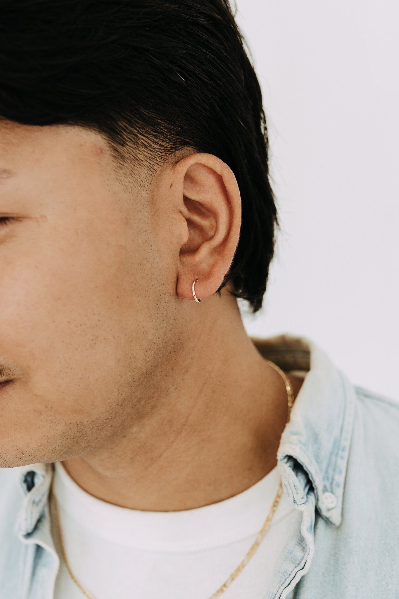 Men's gold sleeper hoop earrings worn with gold chain necklace and denim shirt