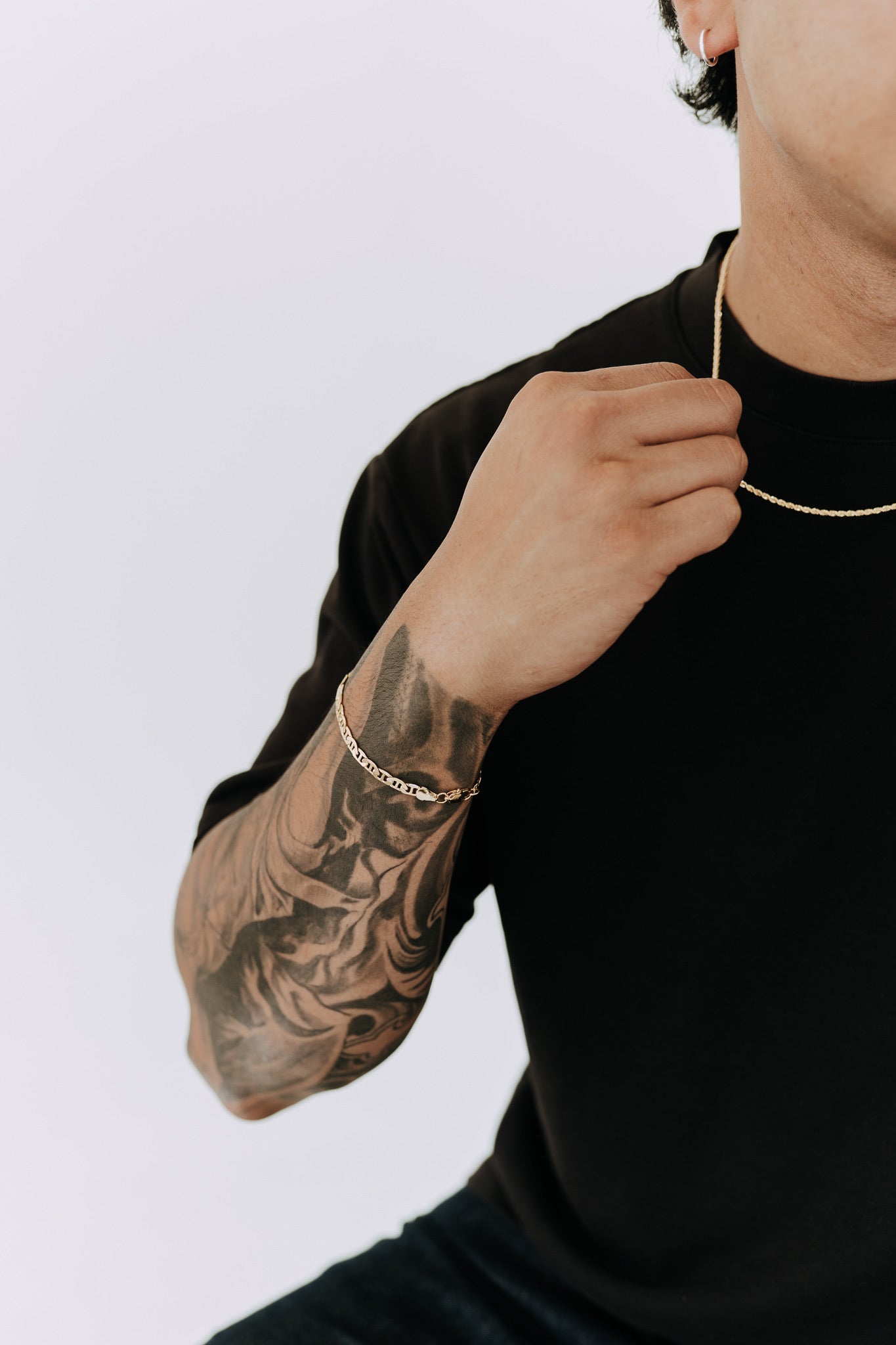 Modern men’s chain bracelet styled with tattoos, neutral tones, and layered accessories
