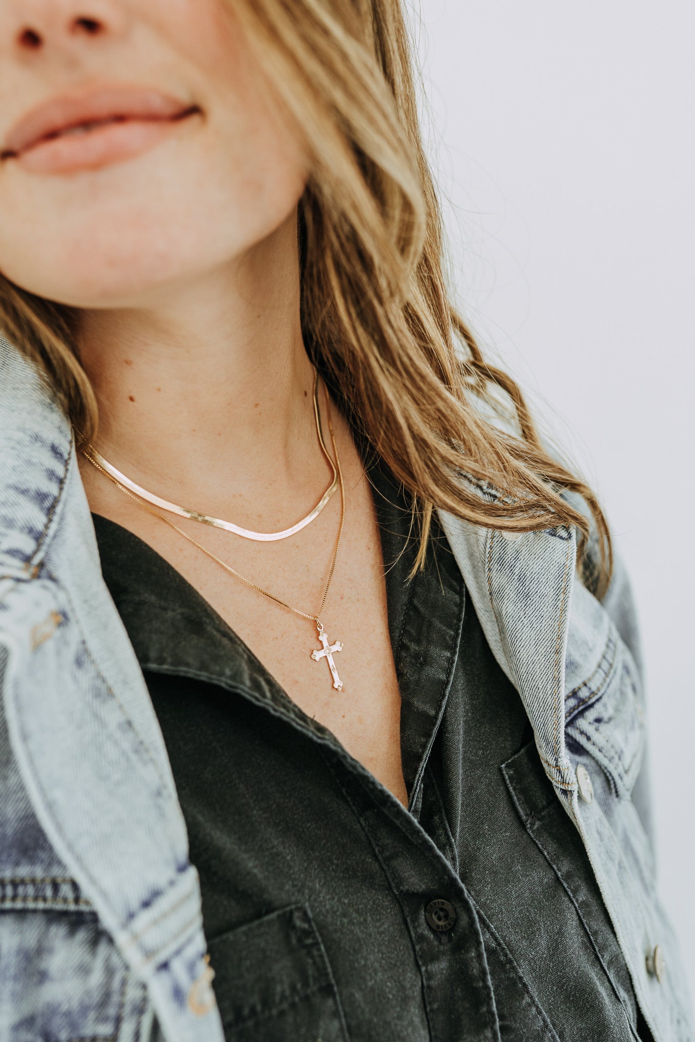 Woman wearing larger gold cross pendant necklace with layered chains