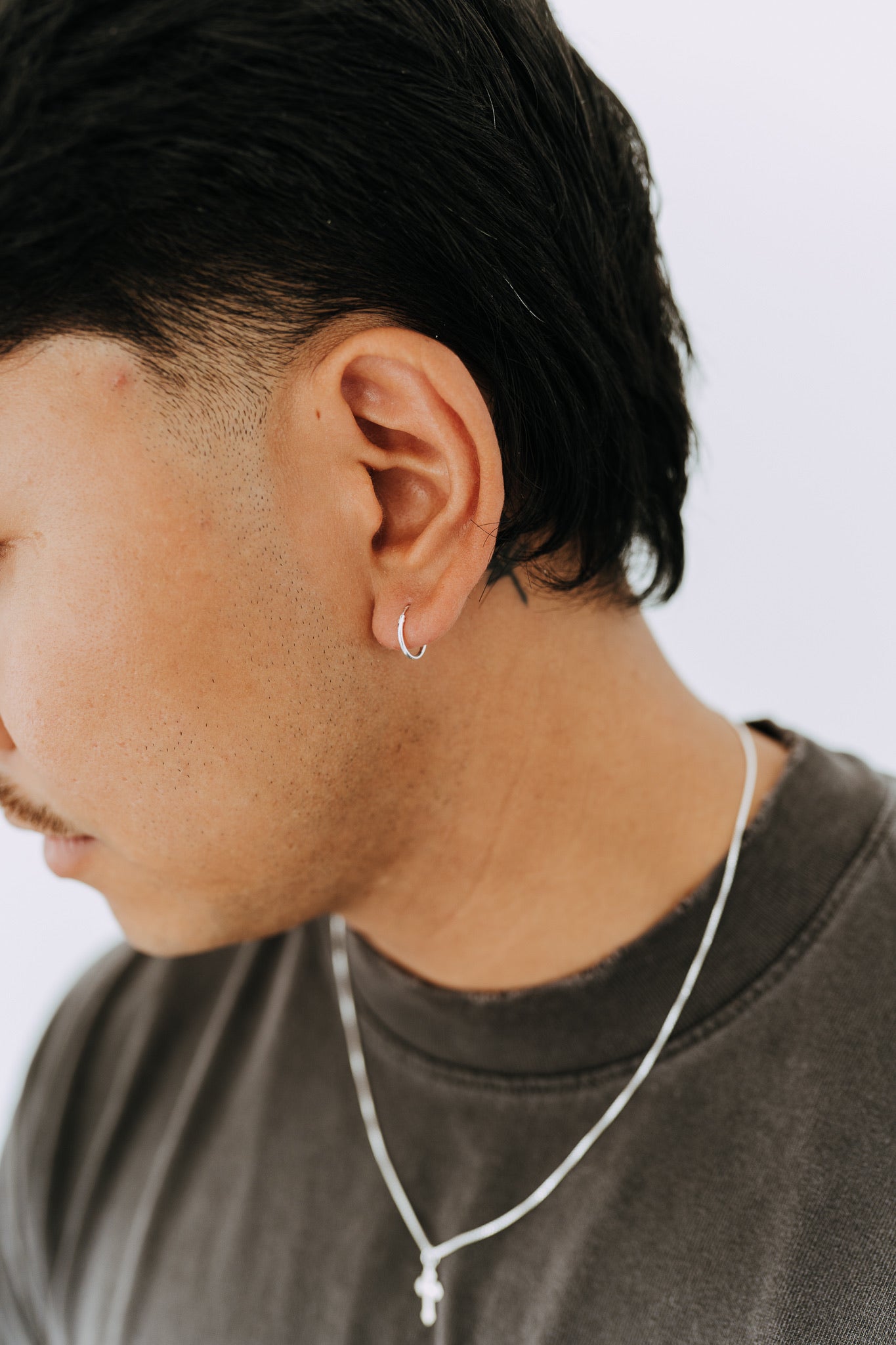 Close-up side profile of a man wearing minimalist sterling silver huggie hoop earrings.