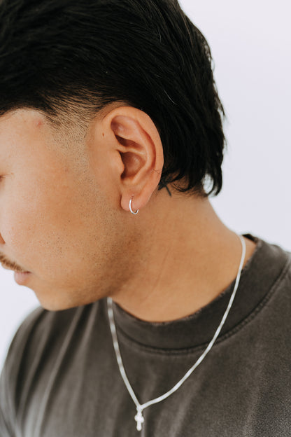 Close-up side profile of a man wearing minimalist sterling silver huggie hoop earrings.