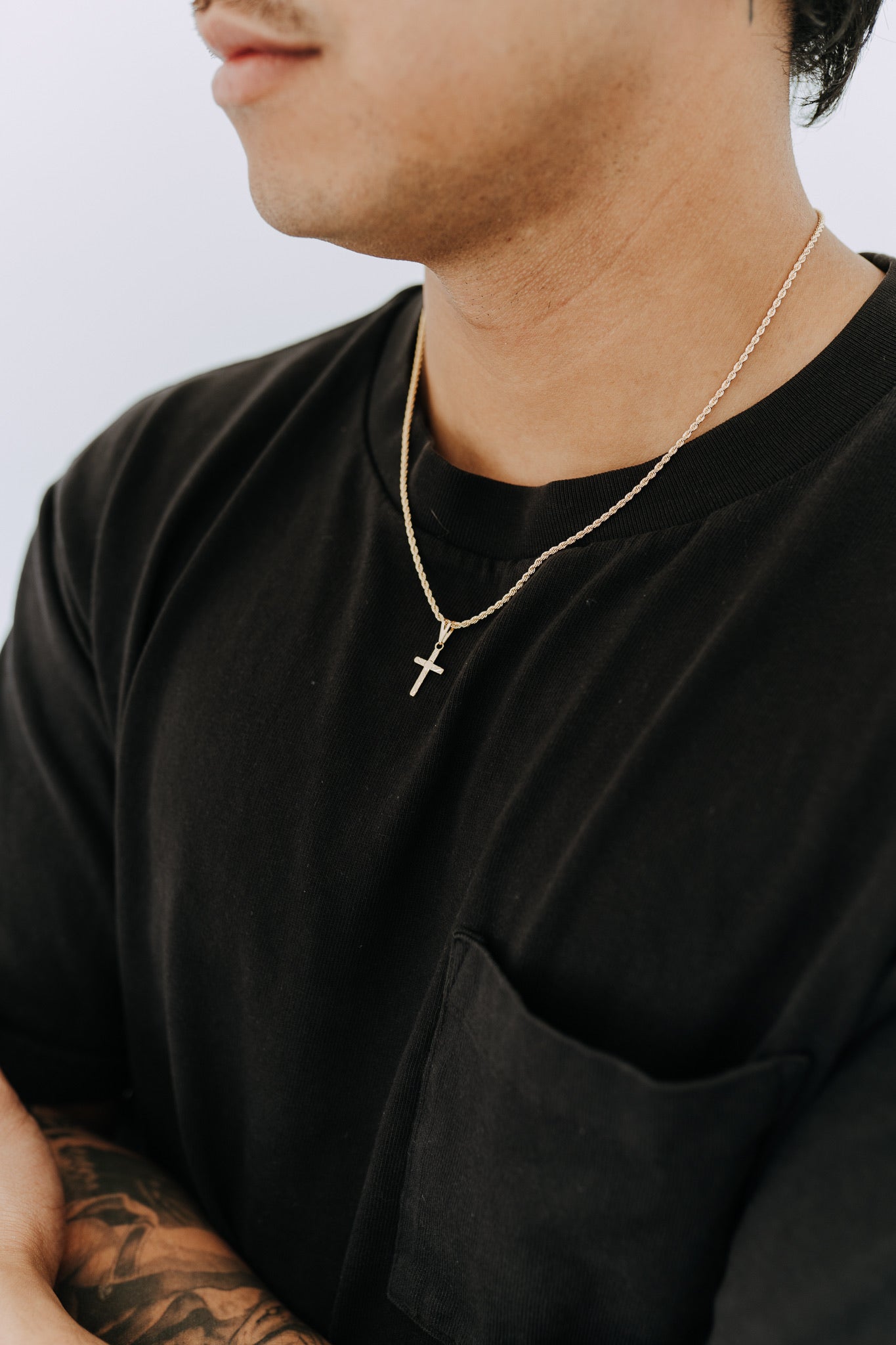 Minimal gold cross necklace for men featuring a detailed engraved pendant and rope chain