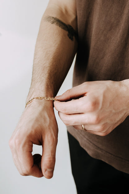 Minimal men’s gold chain bracelet worn casually with dark denim and relaxed streetwear look